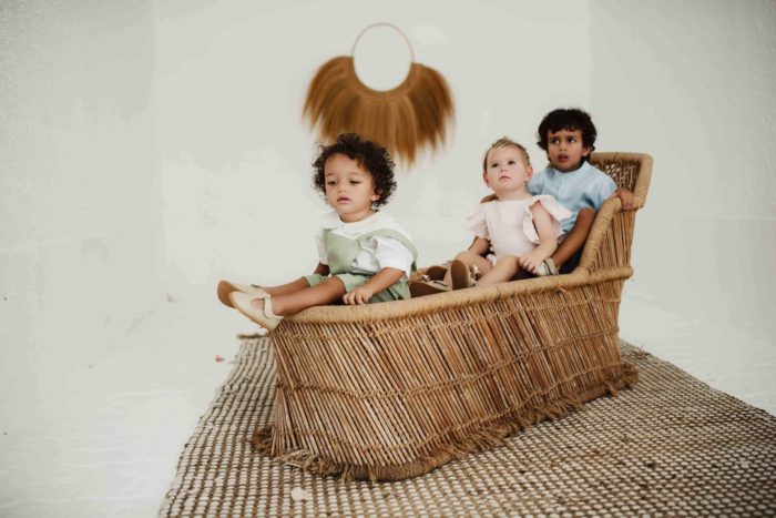 Three cute kids in wicker chair showing off barefoot shoes.